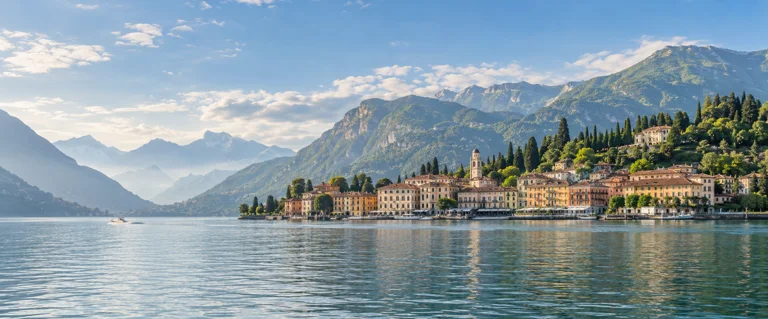 Ochre lakeside buildings and wooded mountains reflected in blue-green Lake Como